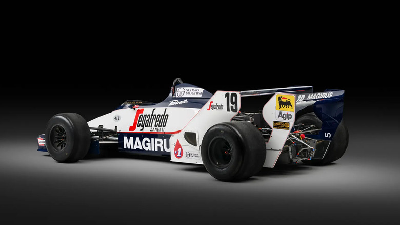 Tričetrtinski pogled od zadaj na Toleman TG183B-05 pod reflektorjem v temnem studiu