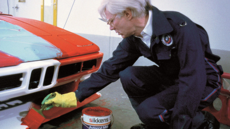 Andy Warhol črta rdeče barve z velikim čopičem po sprednjem odbijaču četrtega avtomobila BMW Art Car.