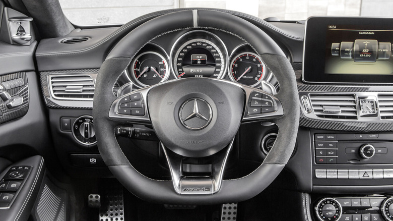 Notranjost vozila Mercedes-Benz CLS 63 AMG iz leta 2014 z analogno-digitalnimi instrumentnimi ploščami spredaj in na sredini. In toliko gumbov.