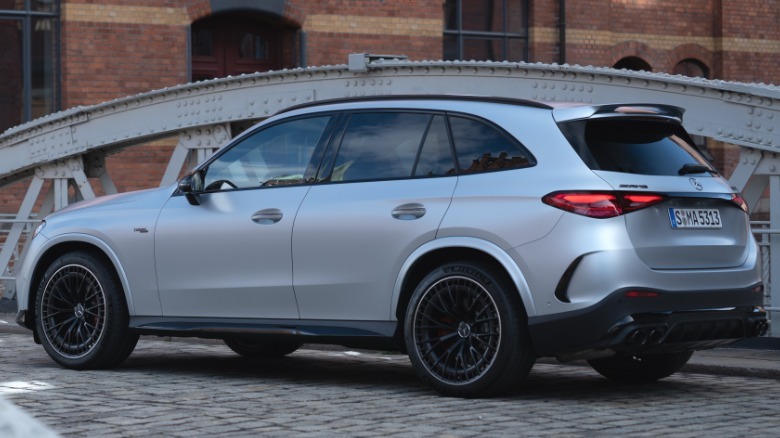 Zadnji tričetrtinski posnetek mat srebrnega športnega terenca AMG GLC53, parkiranega na tlakovanem mostu pred zidano stavbo