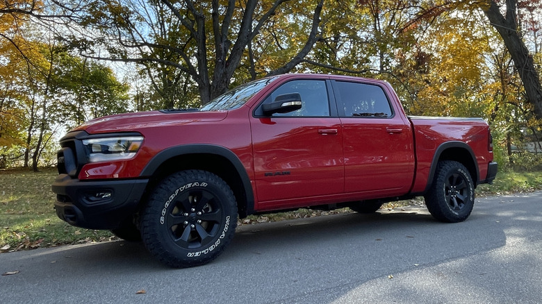 Rdeči Dodge Ram 1500 Rebel 2023 na stranskem cestišču s padajočimi drevesi za njim.