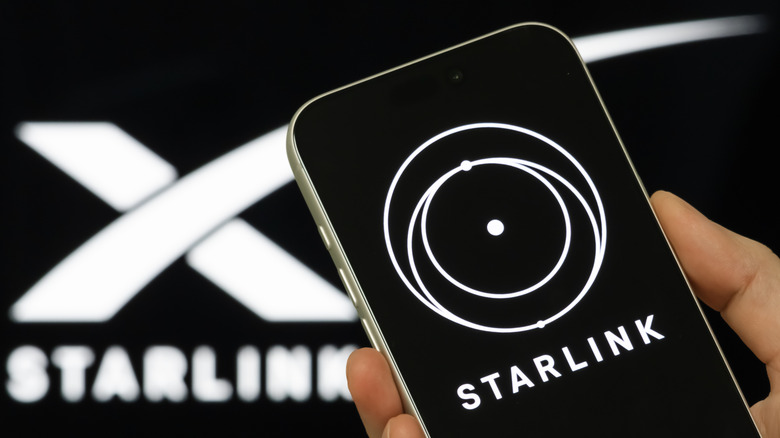 Roka, ki drži telefon z aplikacijo Starlink na zaslonu, z logotipom Starlink v ozadju