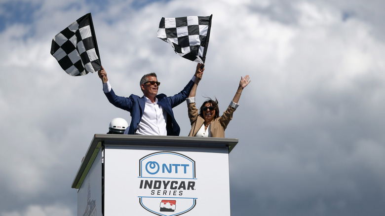Sean Duffy, ameriški minister za promet, stoji na štartni/ciljni tribuni dirke Freedom 250 IndyCar v Washingtonu DC leta 2026 in maha s karirastimi zastavami.