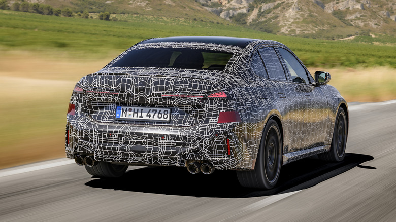 Pogled od zadaj 3/4 kamufliranega 2027 BMW M350 xDrive v gibanju.