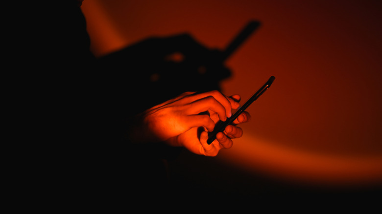 Dve roki uporabljata pametni telefon v dramatični rdeči svetlobi