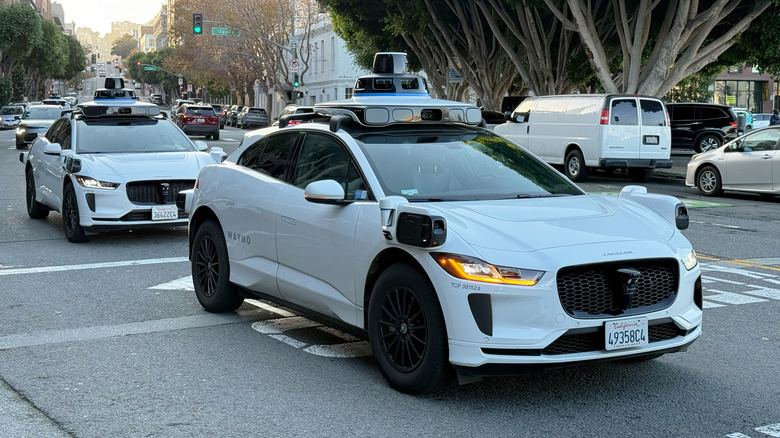 Pogled od spredaj 3/4 dveh robotaksijev Waymo, ki zavijata desno na križišču v mestu