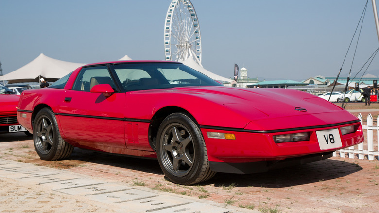 Rdeči Chevrolet Corvette generacije C4, parkiran pred belo ograjo s panoramskim kolesom v ozadju