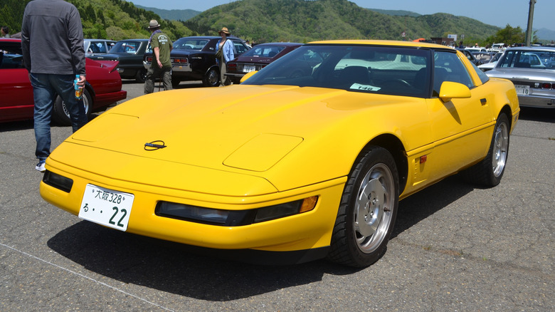 Spredaj levi 3/4 pogled na rumeno C4 Corvette, parkirano na tlakovani površini z drugimi avtomobili v ozadju