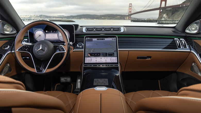 Širok posnetek armaturne plošče v Mercedes-Maybachu S680 iz leta 2026 s temno rjavo notranjostjo in pogledom na most Golden Gate skozi vetrobransko steklo na siv dan