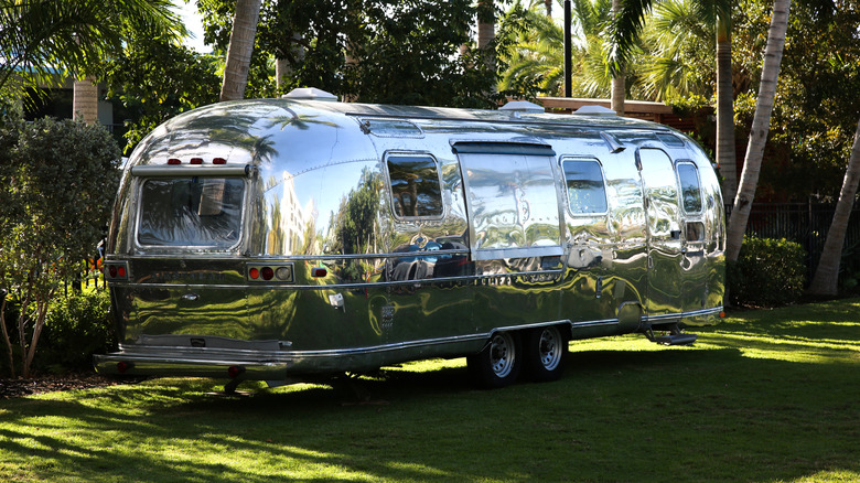 Pogled od zadaj 3/4 potovalne prikolice Airstream, parkirane na travi s palmami za njo
