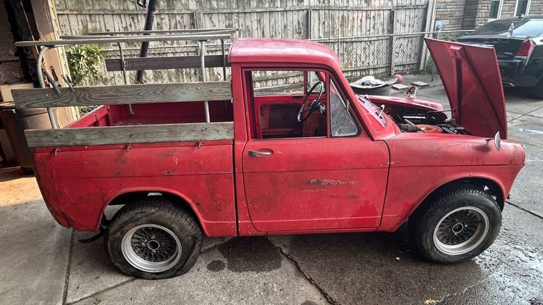 Rdeči tovornjak Daihatsu Hijet z lesenimi stranskimi ograjami na postelji in odprtim pokrovom, parkiran na primestnem dovozu.