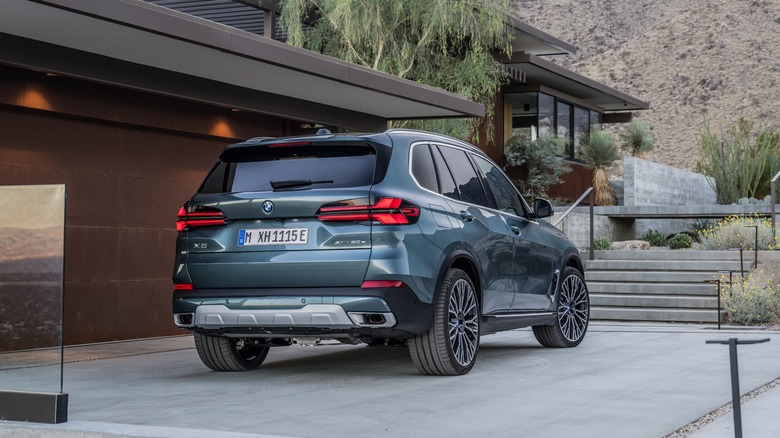 3/4 pogled od zadaj na BMW X5 letnik 2024, parkiran na dovozu hiše v puščavi