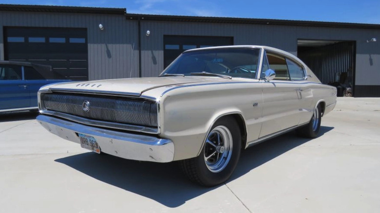 Beli Dodge 426 Hemi Charger iz leta 1966, parkiran na betonu pred veliko garažo.