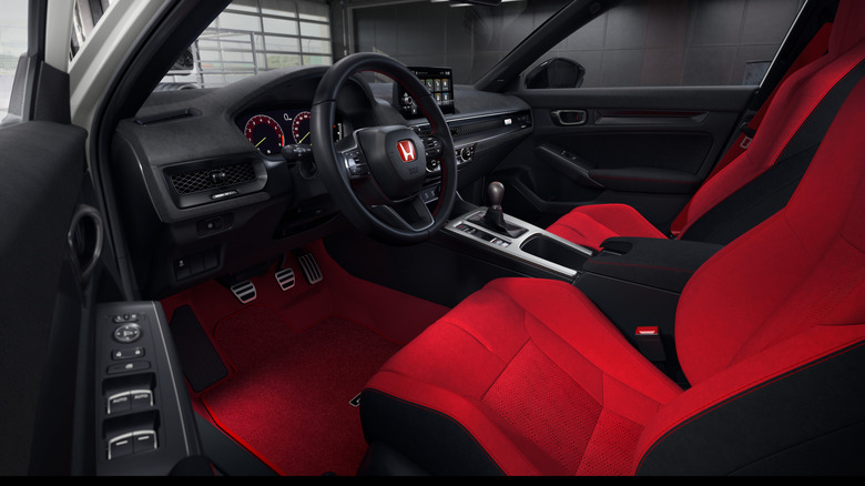 Pogled skozi voznikova vrata na armaturno ploščo v Civic Type R 2027 z rdečimi sedeži in novo armaturno ploščo Ultrasuede