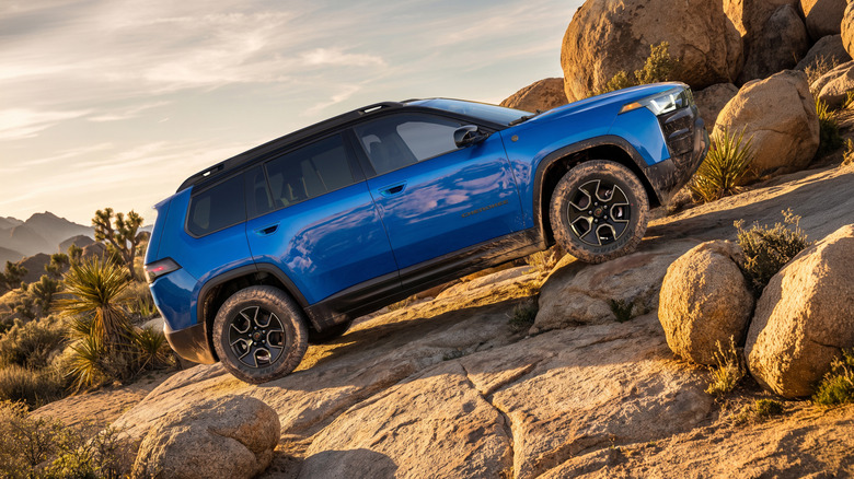 Stranski pogled na modri Cherokee Trailhawk, ki se pelje po skalnem klancu pred Joshua Trees in več skal