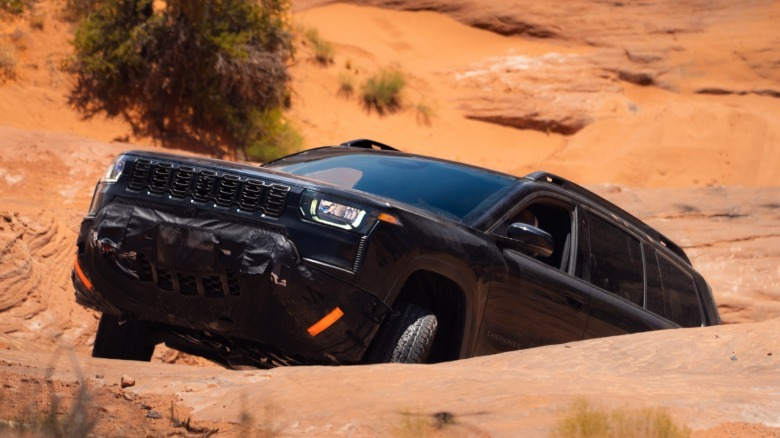 črni cherokee trailhawk, ki se pelje po strmem skalnem klancu, za njim pa se vidi drevo