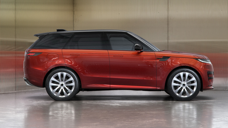 Stranski pogled na rdeči Range Rover Sport, parkiran na svetleči površini pred odsevnimi valovitimi stenami