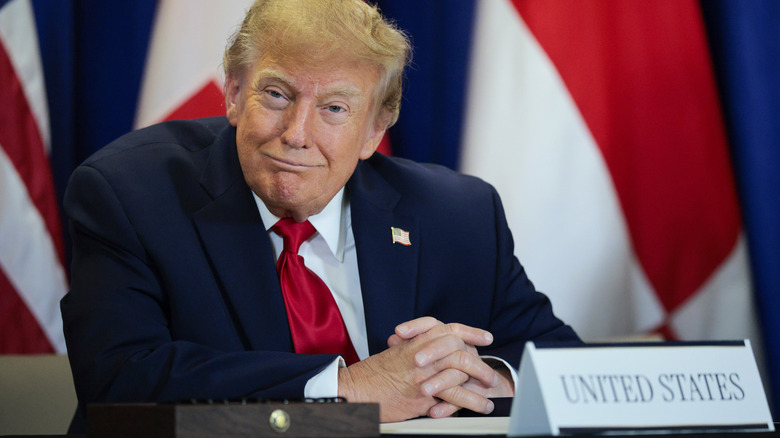 Donald Trump sedi za mizo s prekrižanimi rokami in je videti samozadovoljen