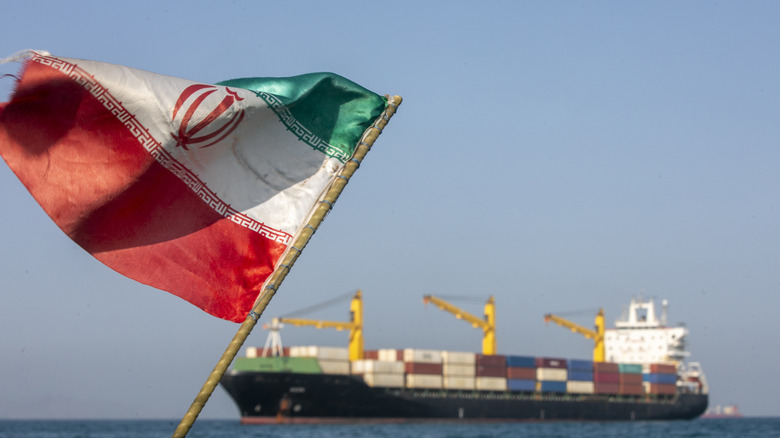 Iranska zastava plapola v vetru, medtem ko ladje ostajajo zasidrane 16. maja 2026 v Hormuški ožini blizu otoka Larak v Iranu.