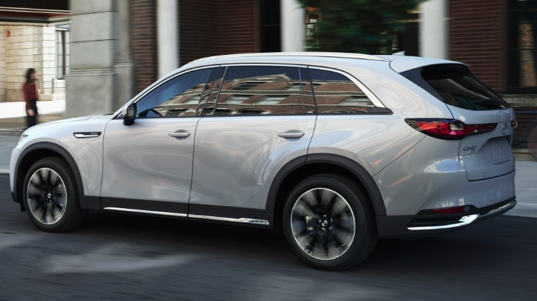 zadnji tričetrtinski posnetek srebrnega CX-90, ki se pelje mimo zidane zgradbe